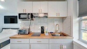Une petite cuisine équipée d’un four à micro-ondes, d’un grille-pain et d’une machine à café, ainsi que d’un évier et d’un lit avec télévision.