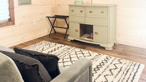 Een kamer met houten wanden, een televisie bevestigd aan een houten balk, een groene dressoir met laden, een klein tafeltje en een kamerbreed tapijt met patroon.