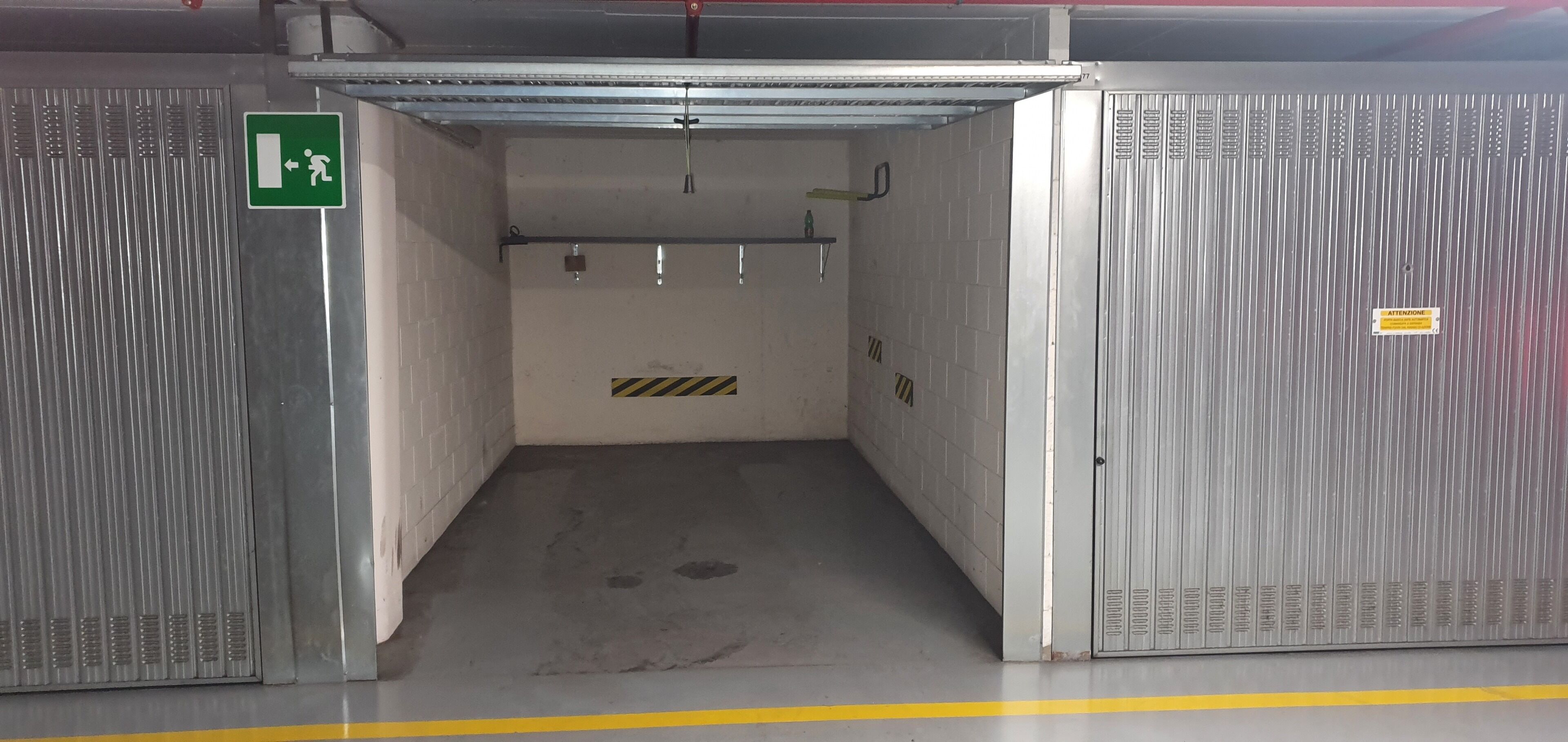 An industrial-style elevator shaft with a green emergency exit sign, a yellow caution stripe, and a metal door with a handle.