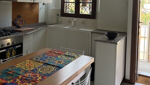 A compact kitchen with white cabinets, a gas stove, a sink, and a window with decorative iron bars. - Cosy centrally located apartment with free of charge garage (Milano)