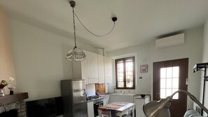 A modern kitchen with white cabinets, a dining table, and a built-in oven. There is a grey sofa and a TV in the living area. - Cosy centrally located apartment with free of charge garage (Milano)