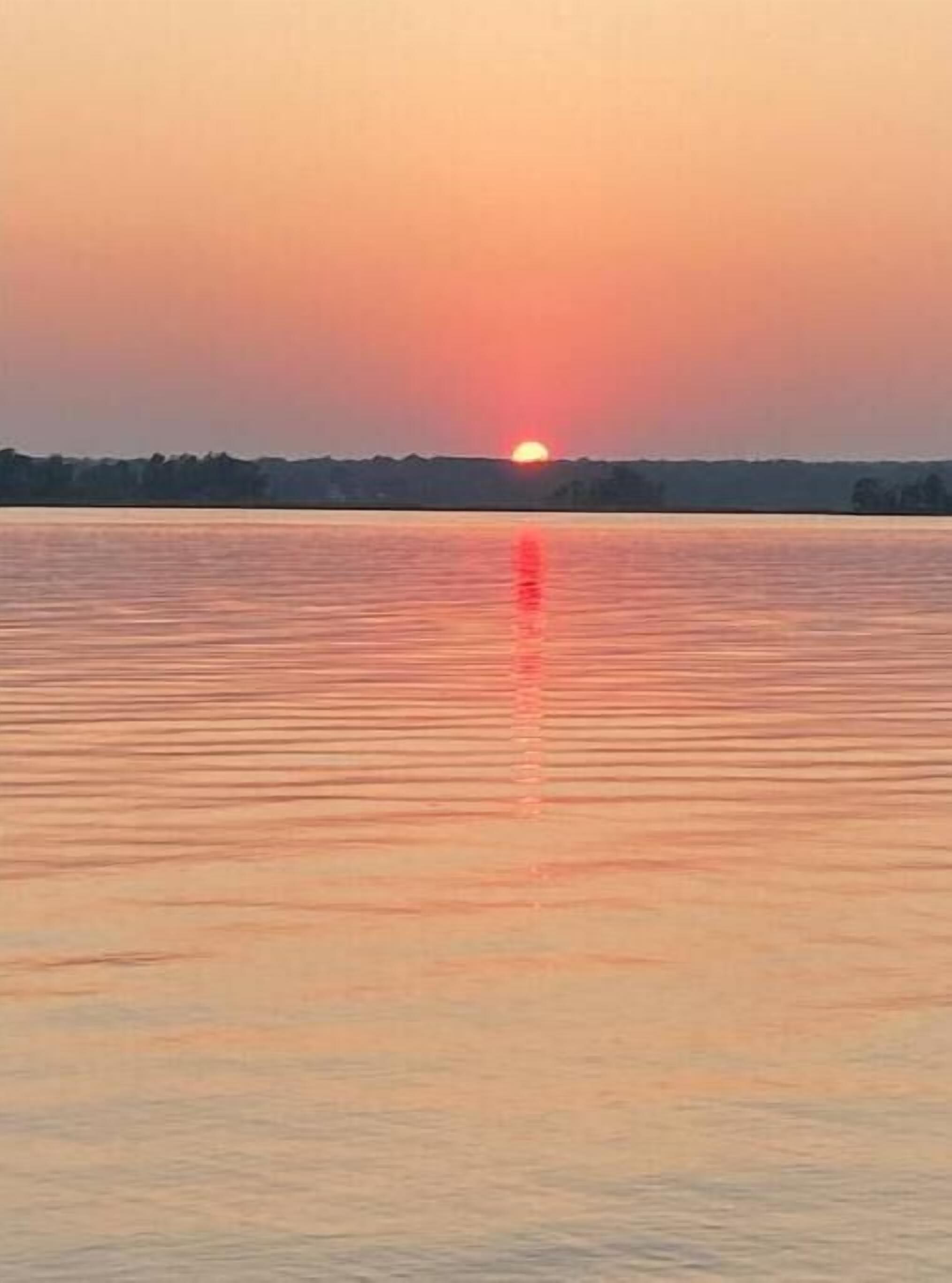 Atardecer sobre una superficie acuática tranquila con una costa lejana.