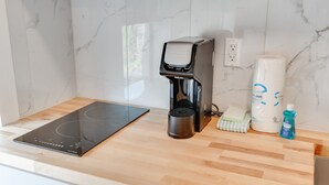 A kitchen with a black induction cooktop, a coffee maker, a roll of paper towels, a bottle of dish soap, and a cloth.