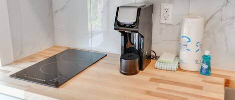 A kitchen with a black induction cooktop, a coffee maker, a roll of paper towels, a bottle of dish soap, and a cloth.