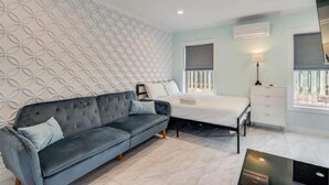 A modern bedroom with a grey sofa, a bed, a dresser, and patterned wallpaper.
