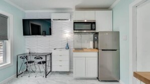A compact kitchen with white cabinets, a stainless steel refrigerator, a microwave, and a small dining area with a table and chairs.