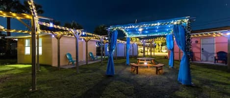 Un patio al aire libre con luces colgantes, una mesa de madera y cortinas azules.