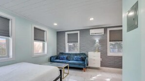 Een slaapkamer met een bed, een blauwe bank, een witte dressoir en een airconditioner.