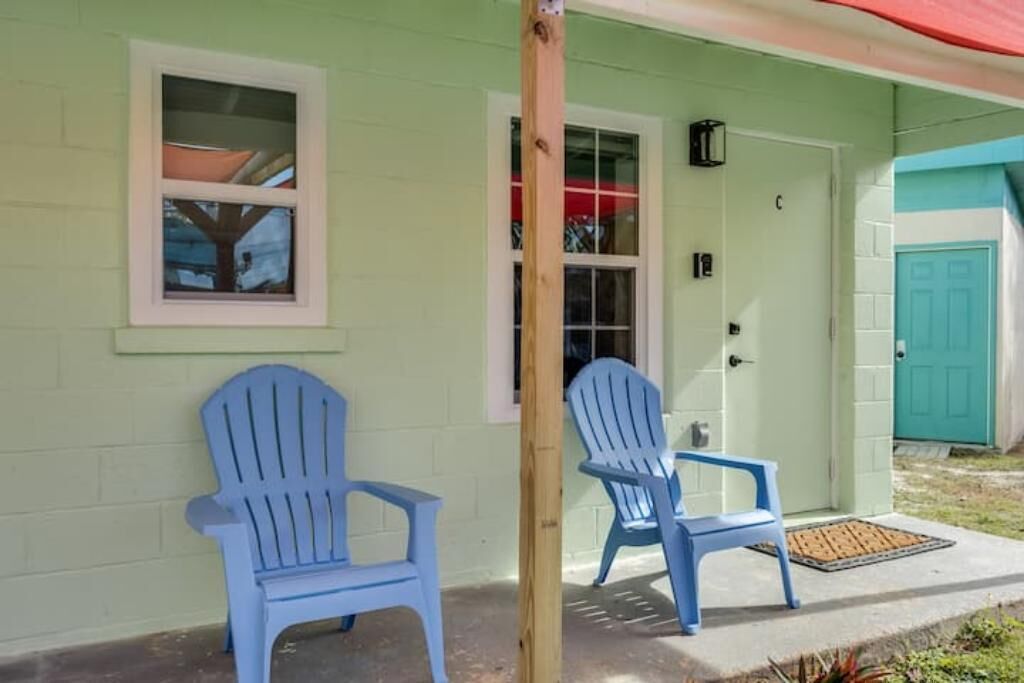 Een lichtgroen gebouw met twee blauwe Adirondack-stoelen ervoor.