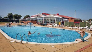 Une piscine dotée d’une zone abritée, de chaises longues et, au fond, d’un bâtiment avec un toit rouge.