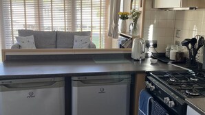 Une cuisine compacte équipée d’un lave-vaisselle intégré, d’une cuisinière et d’une fenêtre avec des stores.