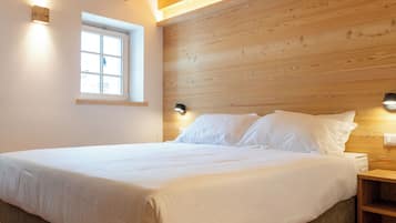 Ein Schlafzimmer mit Holzboden, einem Bett mit weißer Bettwäsche, einem Nachttisch und einer Wandleuchte.
