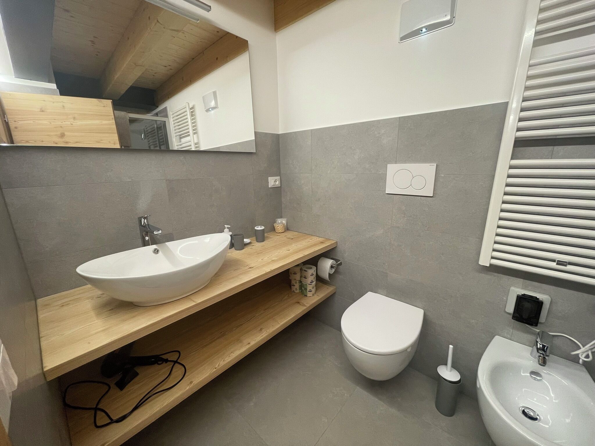 A modern bathroom with a wooden vanity, a white sink, a toilet, and a bidet.