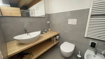 A modern bathroom with a wooden vanity, a white sink, a toilet, and a bidet.