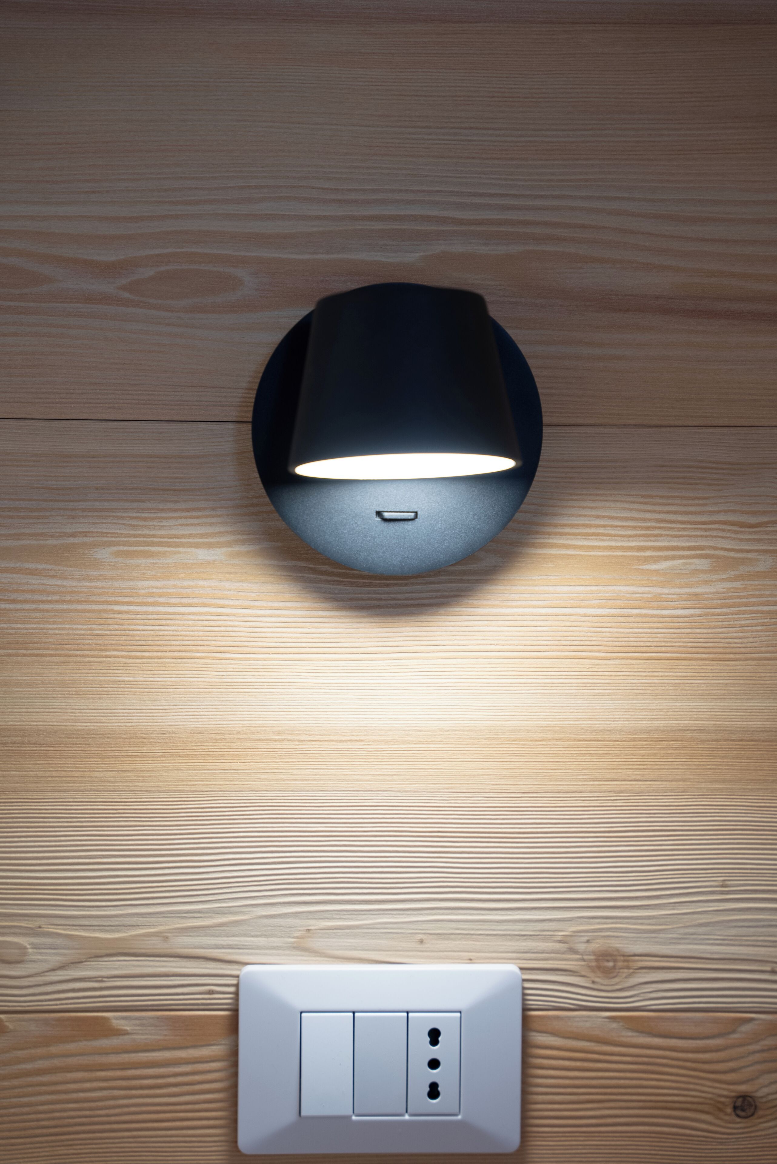 A modern light fixture on a wooden floor with a wall switch below it.