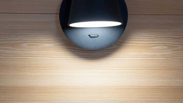 A modern light fixture on a wooden floor with a wall switch below it.