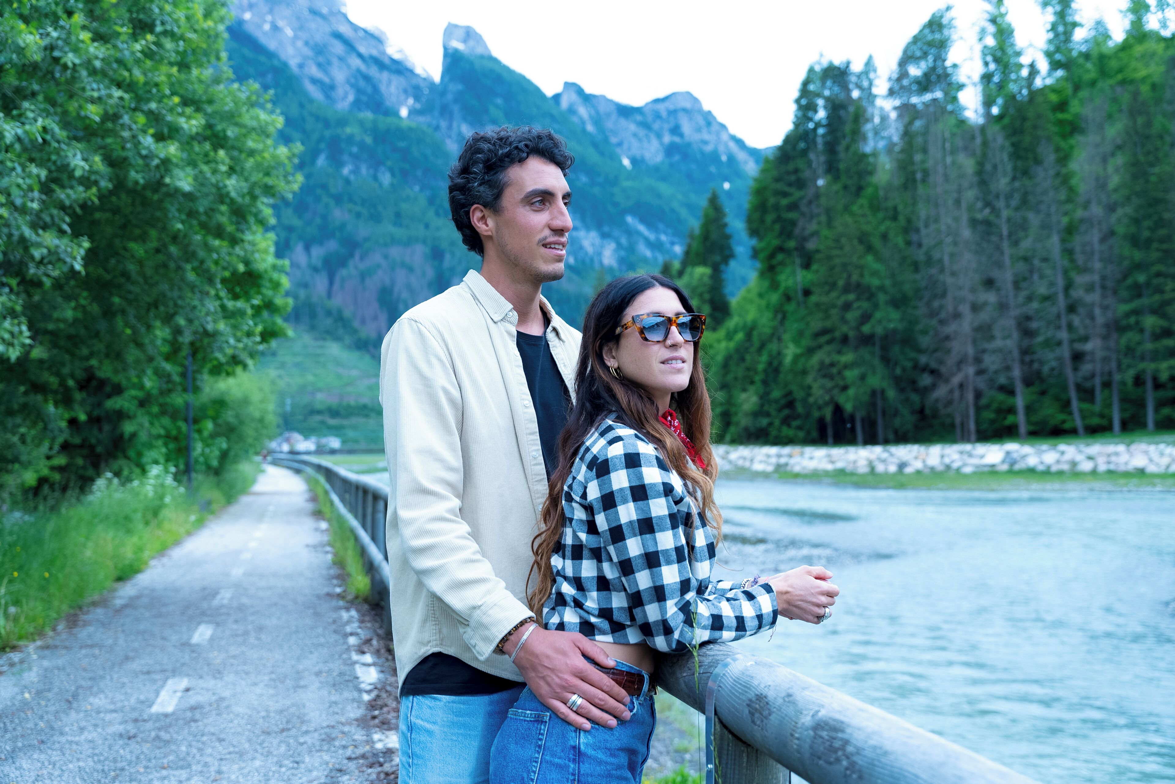 A couple standing by a river with mountains in the background.