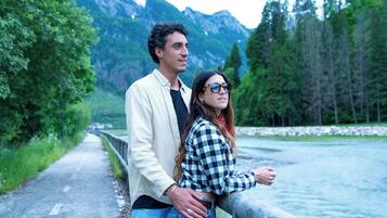 A couple standing by a river with mountains in the background.