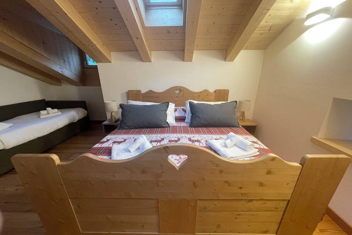A wooden bed with a heart-shaped design, a sofa, and a nightstand with a lamp.