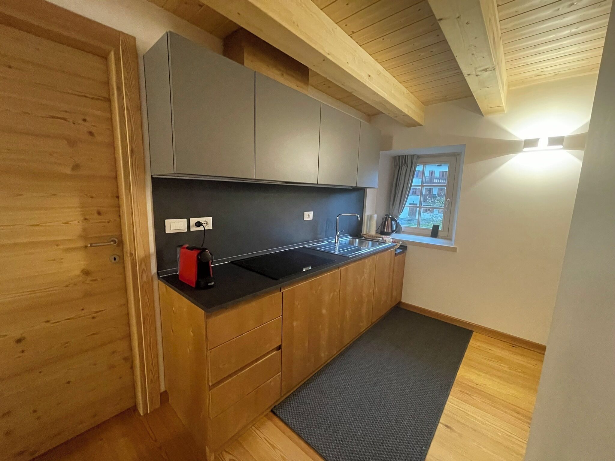 A compact kitchen with wooden cabinets, a black countertop, and a window with a view.