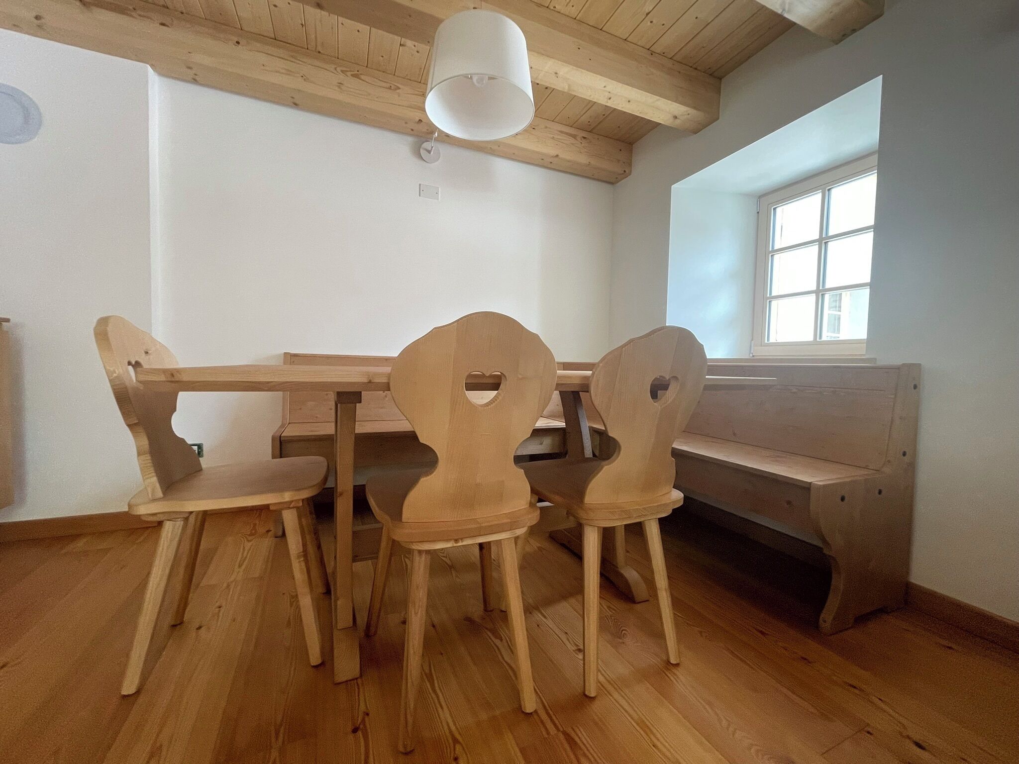 A wooden dining table with four chairs, a bench, and a window with blinds.