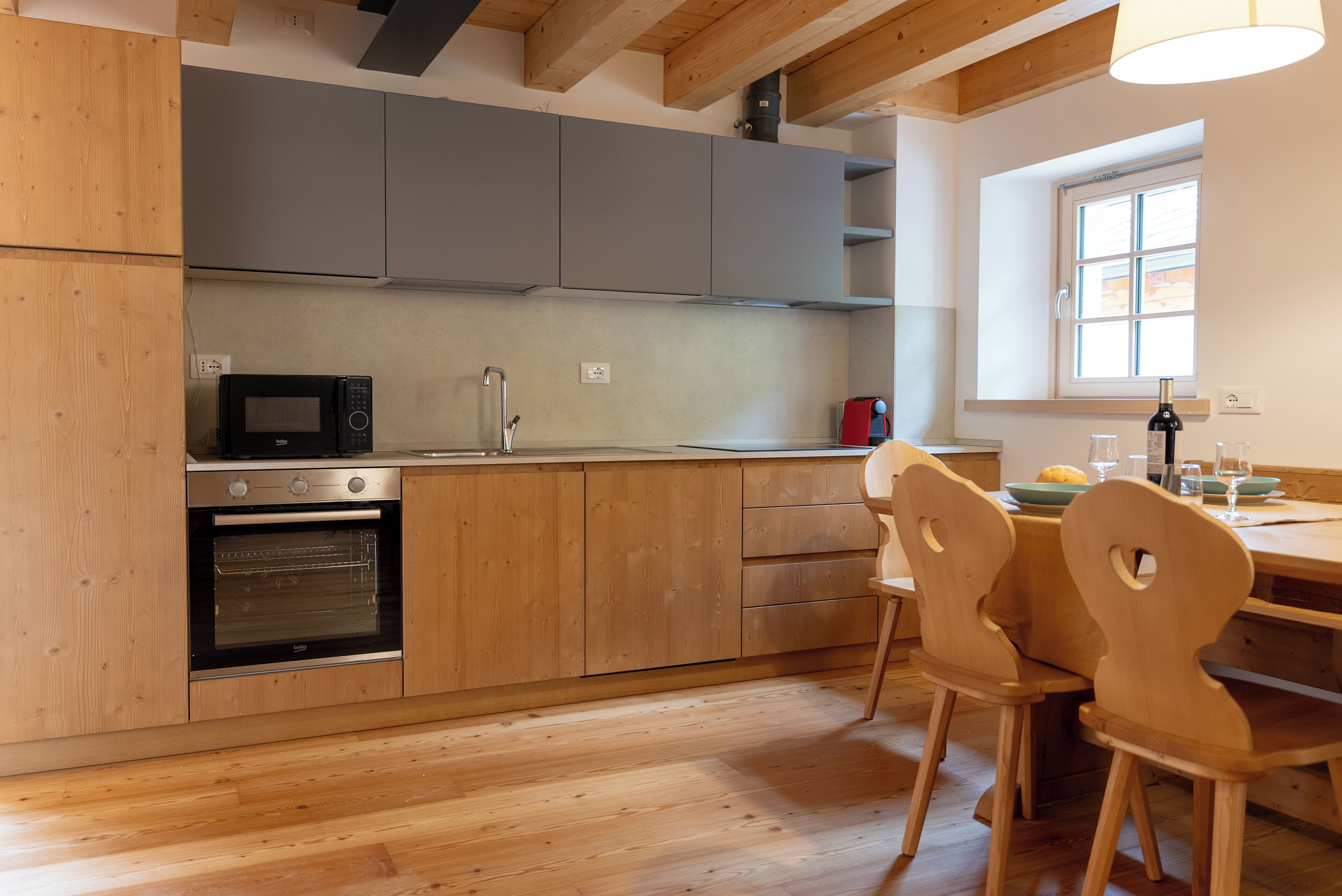 A modern kitchen with wooden cabinets, a built-in oven, a microwave, and a dining area with wooden chairs.