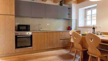 A modern kitchen with wooden cabinets, a built-in oven, a microwave, and a dining area with wooden chairs.