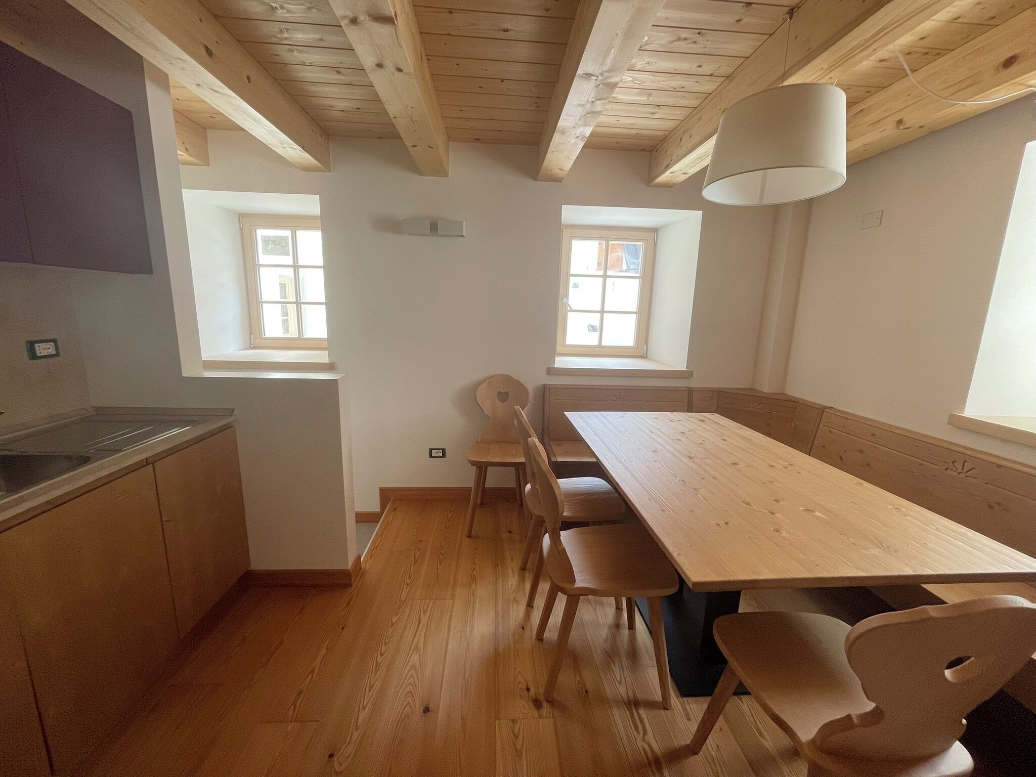 Uma cozinha com armários de madeira, uma mesa comprida e duas janelas.