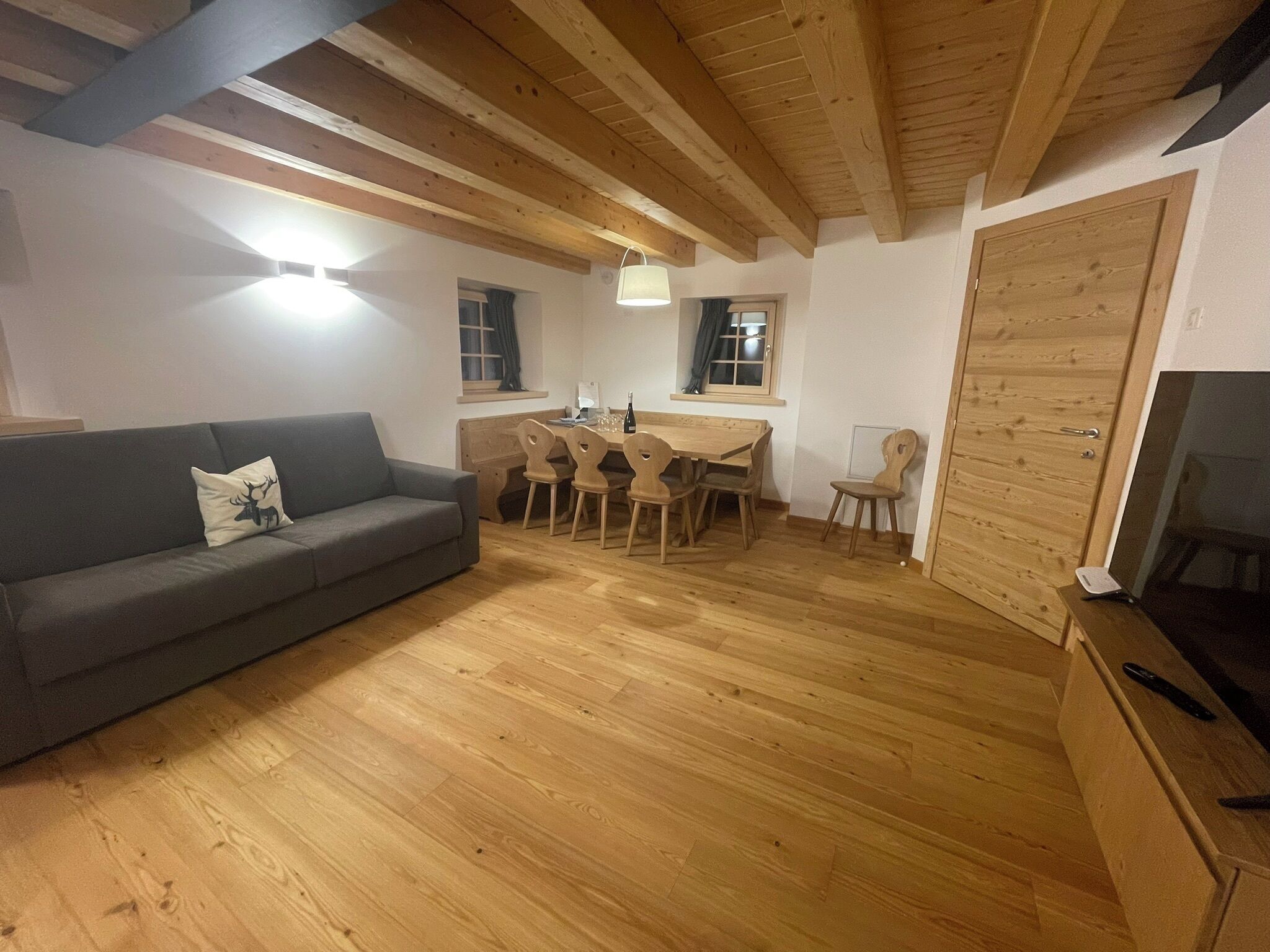 Een gezellige woonkamer met een grijze bank, een houten eettafel en stoelen.