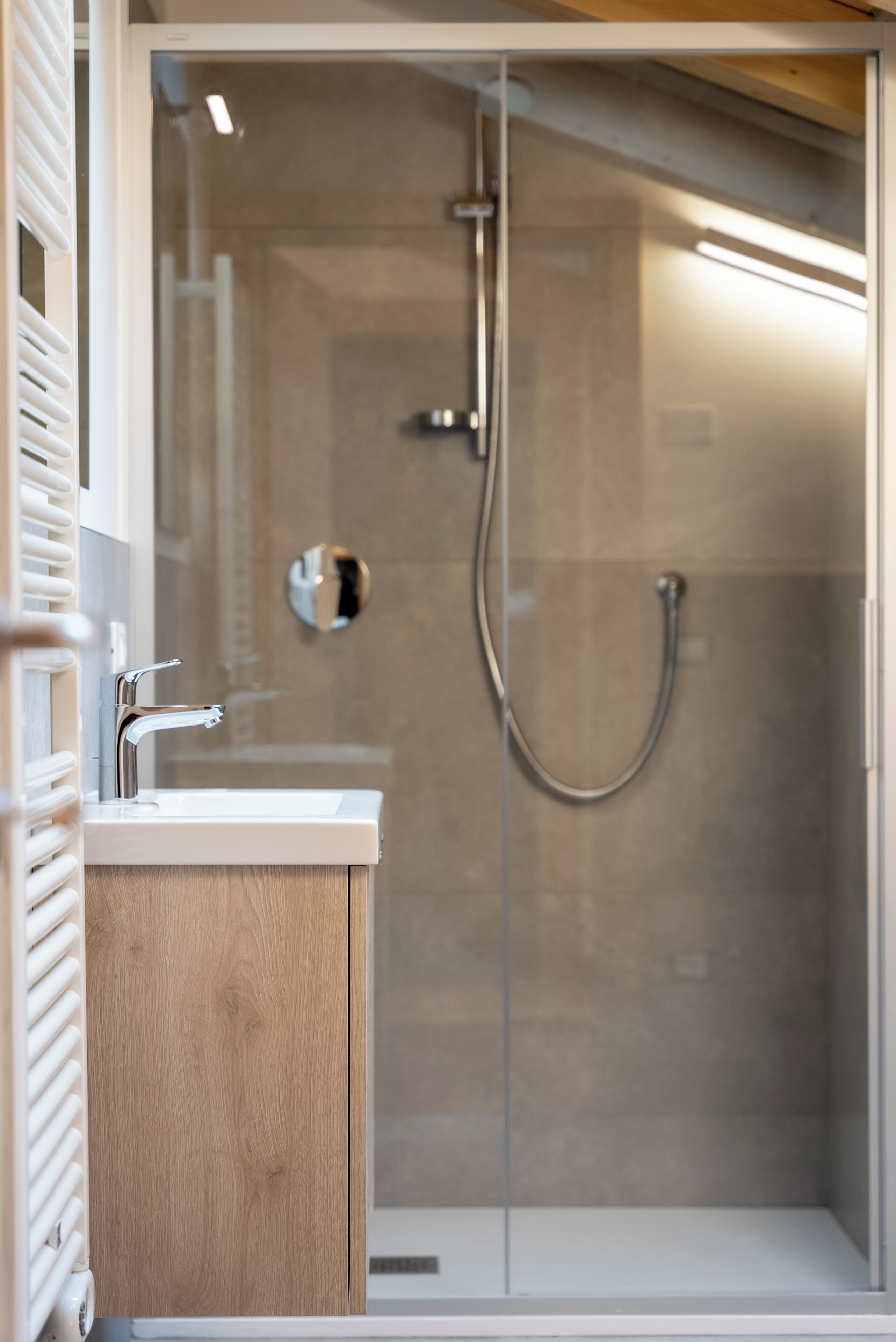 Un baño moderno con ducha envuelta en vidrio, tocador de madera y lavamanos blanco.