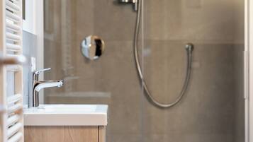 Un baño moderno con ducha envuelta en vidrio, tocador de madera y lavamanos blanco.