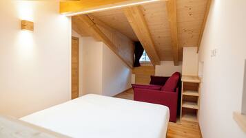 Une chambre avec un plafond en bois, un lit, une chaise rouge et une étagère en bois.