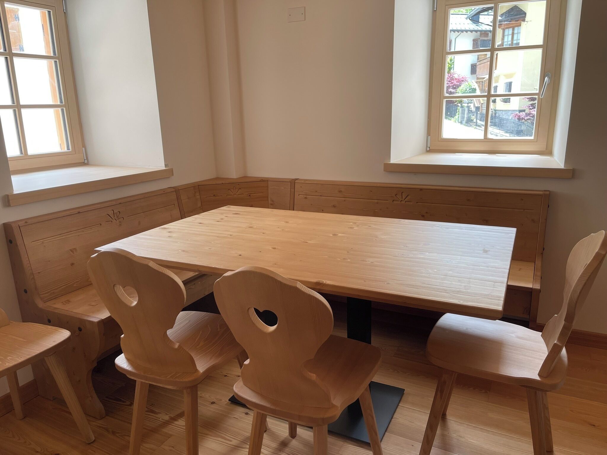 A room with a wooden table and four chairs, a bench along the wall, and windows with views of buildings and greenery.