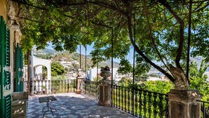 A balcony with a stone floor, a metal railing, and a view of a town and hills in the distance. - Villa di Charme Vicino al Centro (Lipari)