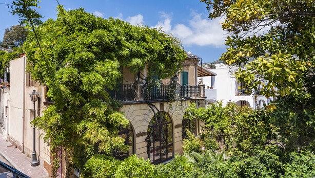 A building with a balcony, arched windows, and lush greenery. - Villa di Charme Vicino al Centro (Lipari)