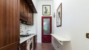 A narrow kitchen with wooden cabinets, a gas stove, and a red door. - Villa di Charme Vicino al Centro (Lipari)