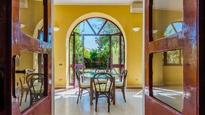 A dining area with a round table and chairs, a yellow wall, and a view of greenery through an arched window. - Villa di Charme Vicino al Centro (Lipari)