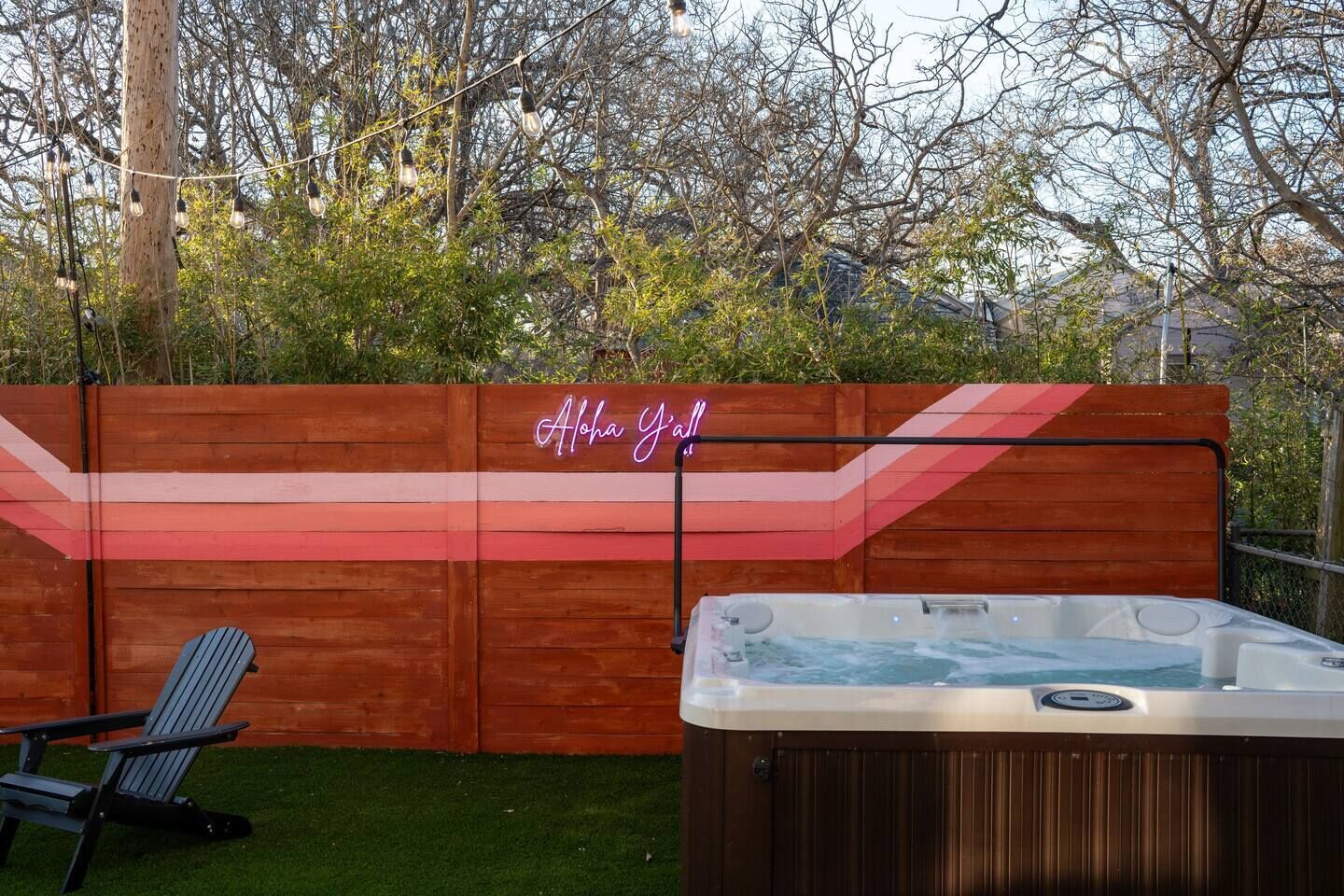 A wooden fence with a neon sign reading "Aloha Yall!" and a hot tub in front.