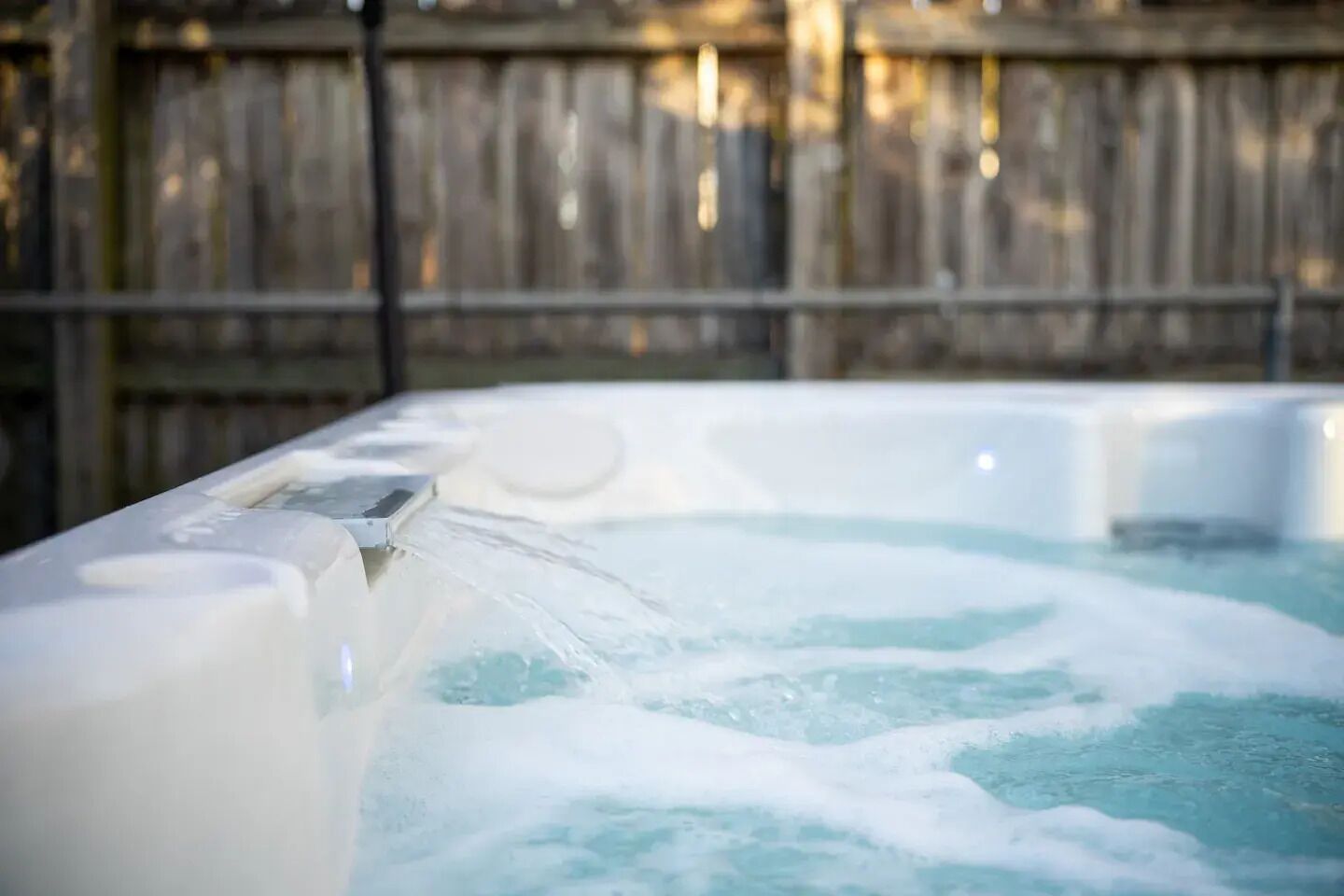 A hot tub with water flowing out, surrounded by a wooden fence.