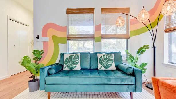 A teal sofa with leaf-patterned cushions, a white door, and a colorful abstract wall. - Hot Tub - E. Austin - 5 min to UT - 10 min to DT

 (Austin)