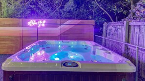 A hot tub with a control panel, surrounded by a wooden fence and a neon sign in the background. - Hot Tub - E. Austin - 5 min to UT - 10 min to DT

 (Austin)