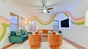 A living room with a teal sofa, orange armchairs, a white rug, and a ceiling fan. - Hot Tub - E. Austin - 5 min to UT - 10 min to DT

 (Austin)