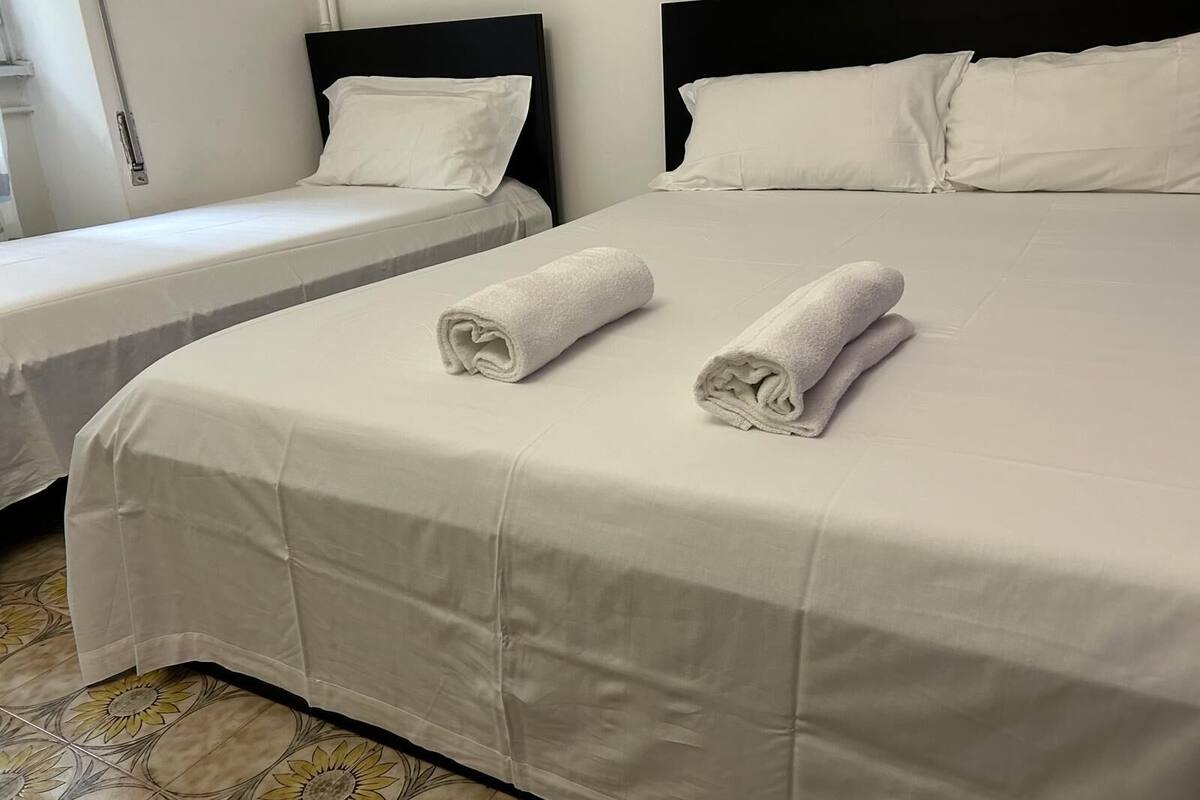 A hotel room with two single beds and a larger bed, all with white linens and pillows.