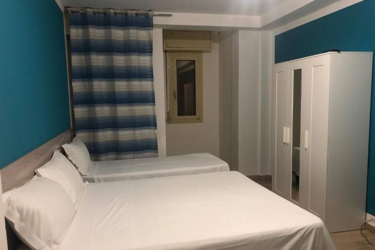 A bedroom with two beds, a wardrobe, and a window with a curtain.