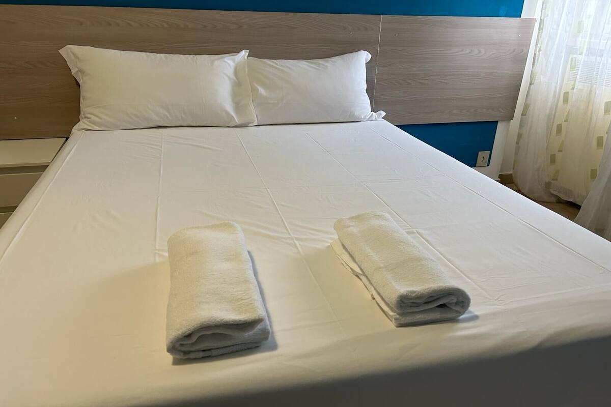 A neatly made bed with white linens and two folded towels on the bed.