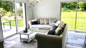Een moderne woonkamer met een bank, salontafel en een groot raam van vloer tot plafond met uitzicht op een gazon.