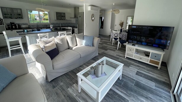 Een moderne woonkamer met een witte bank, een glazen salontafel en een televisie op een standaard.