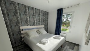 Een moderne slaapkamer met een houten hoofdeinde, een groot bed met witte lakens en uitzicht op groen door een raam.