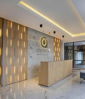 A modern reception area with a marble wall, a wooden reception desk, and a glass partition.