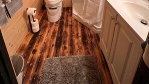Een kleine houten badkamer met toilet, douche en wastafel.